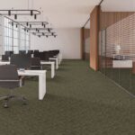 Open office interior with green Pentz Carpet, rows of white desks and black chairs, and floor-to-ceiling windows along the left wall.