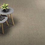 A textured beige Pentz Carpet with two nested gray side tables, one holding a small potted plant and the other a black notebook, shown on a neutral floor.
