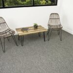 A gray Pentz Carpet floor in a minimalist room with two wire chairs and a small wooden table beneath a window.